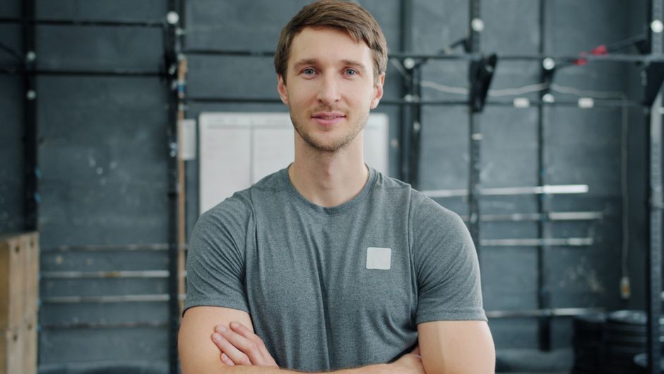 Man confidently posing indoors with crossed arms in a gym setting.